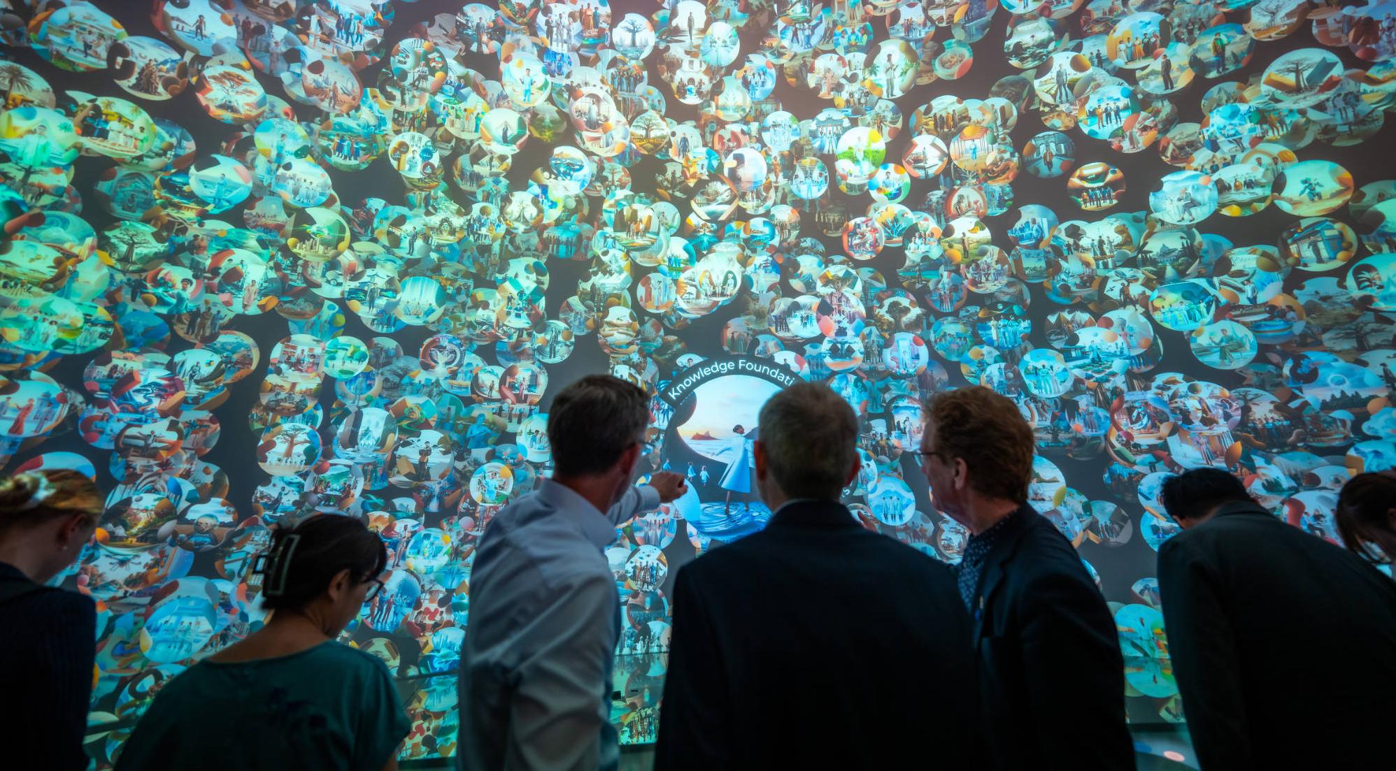 Inside the Swiss Pavilion at Expo 2025 in Osaka people looking and pointing at a gigantic screen with images within bubbles.